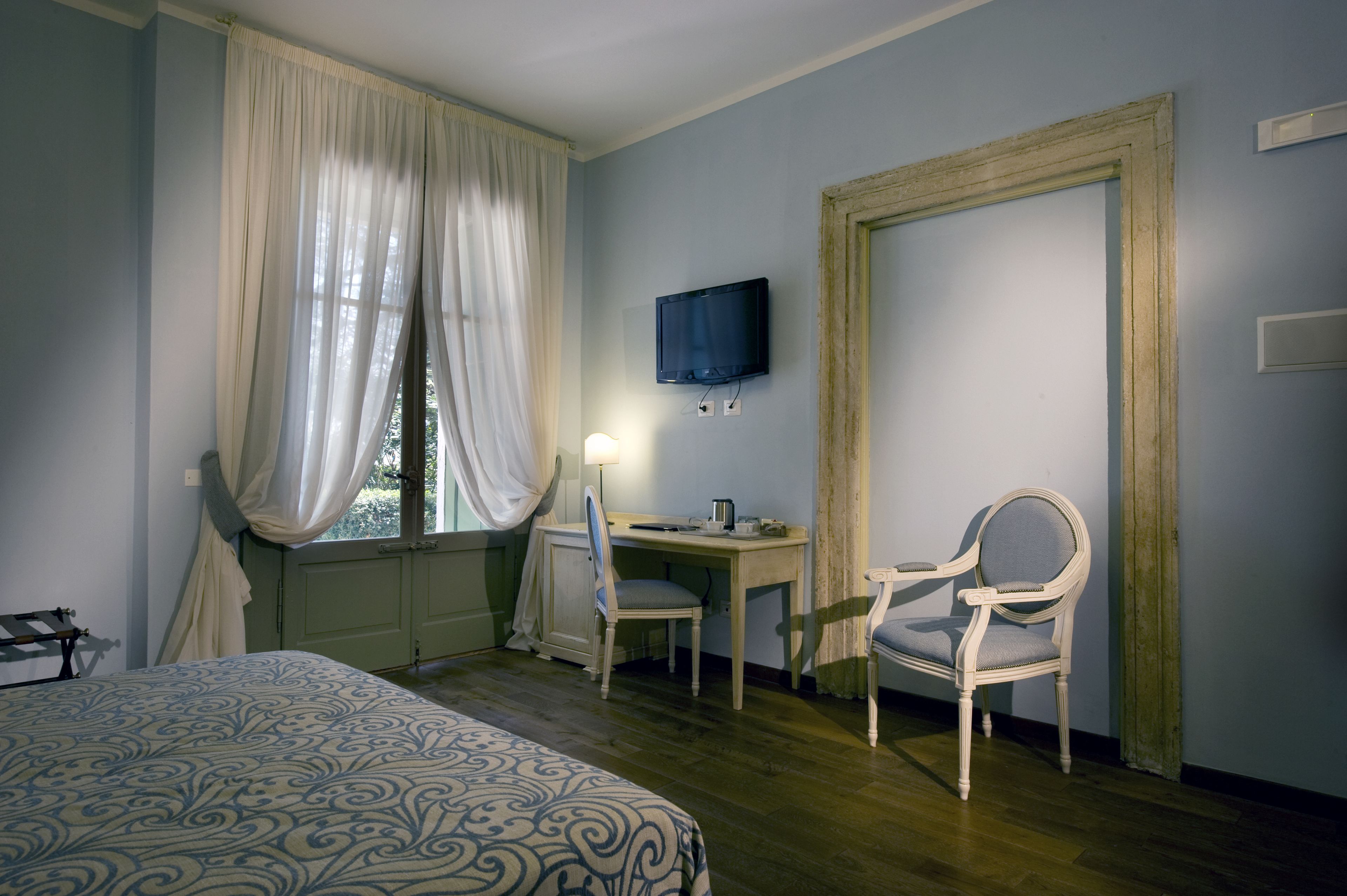 Ein Hotelzimmer mit einem Bett, einem Schreibtisch, zwei Stühlen, einem Fernseher und einem Fenster mit Vorhängen.