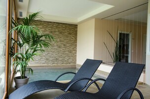 Un área junto a la piscina con dos sillas de descanso, una planta en maceta y un muro de piedra.
