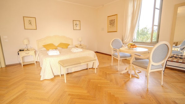 A bedroom with a bed, bedside tables, a bench, a round table with chairs, and framed pictures on the walls. - Relais Corte Cavalli (Ponti sul Mincio)