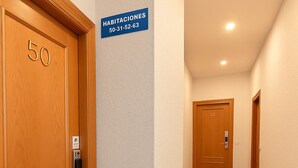 Un pasillo con puertas de madera, números 50 y 32, un cartel que indica 'Habitaciones' con un número de teléfono y una señalización de estacionamiento P.