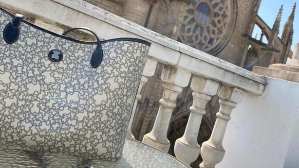 Una mesa redonda con un mantel estampado y un par de gafas de sol, frente a un edificio histórico de arquitectura detallada.