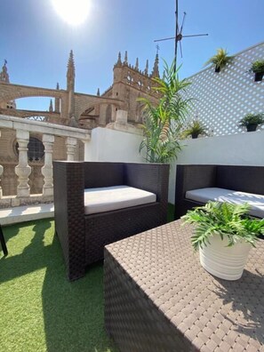 A rooftop patio with wicker furniture, a potted plant, and a view of a historic building. - Catedral Boutique (Seville)