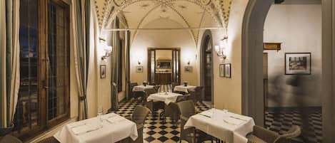 Un comedor con piso de cuadros, mesas cubiertas con manteles blancos y sillas de mimbre.