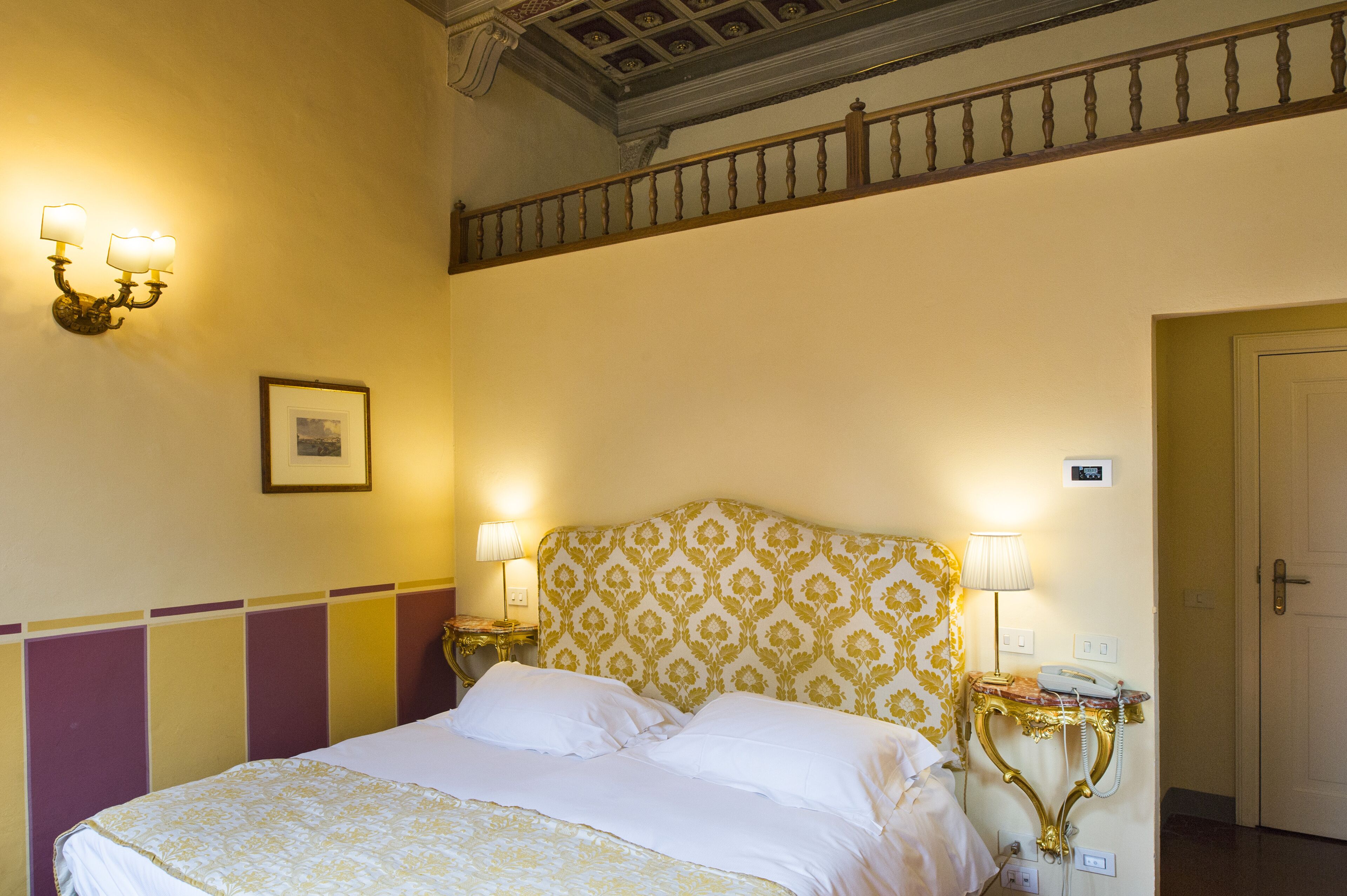 A hotel room with a bed, two bedside lamps, a framed picture on the wall, and a door.