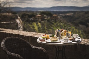 Una mesa con alimentos para el desayuno y una silla de mimbre, con vistas a un paisaje pintoresco.