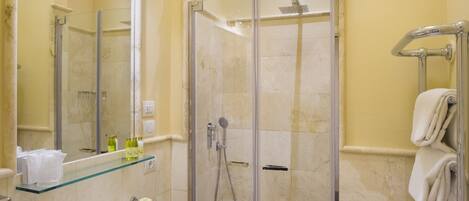 A modern bathroom with a glass-enclosed shower, a glass shelf with toiletries, and a white sink.