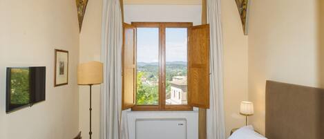 Une chambre d’hôtel comprenant un lit, un bureau, une chaise, une fenêtre avec des rideaux, une lampe et une vue sur le paysage.