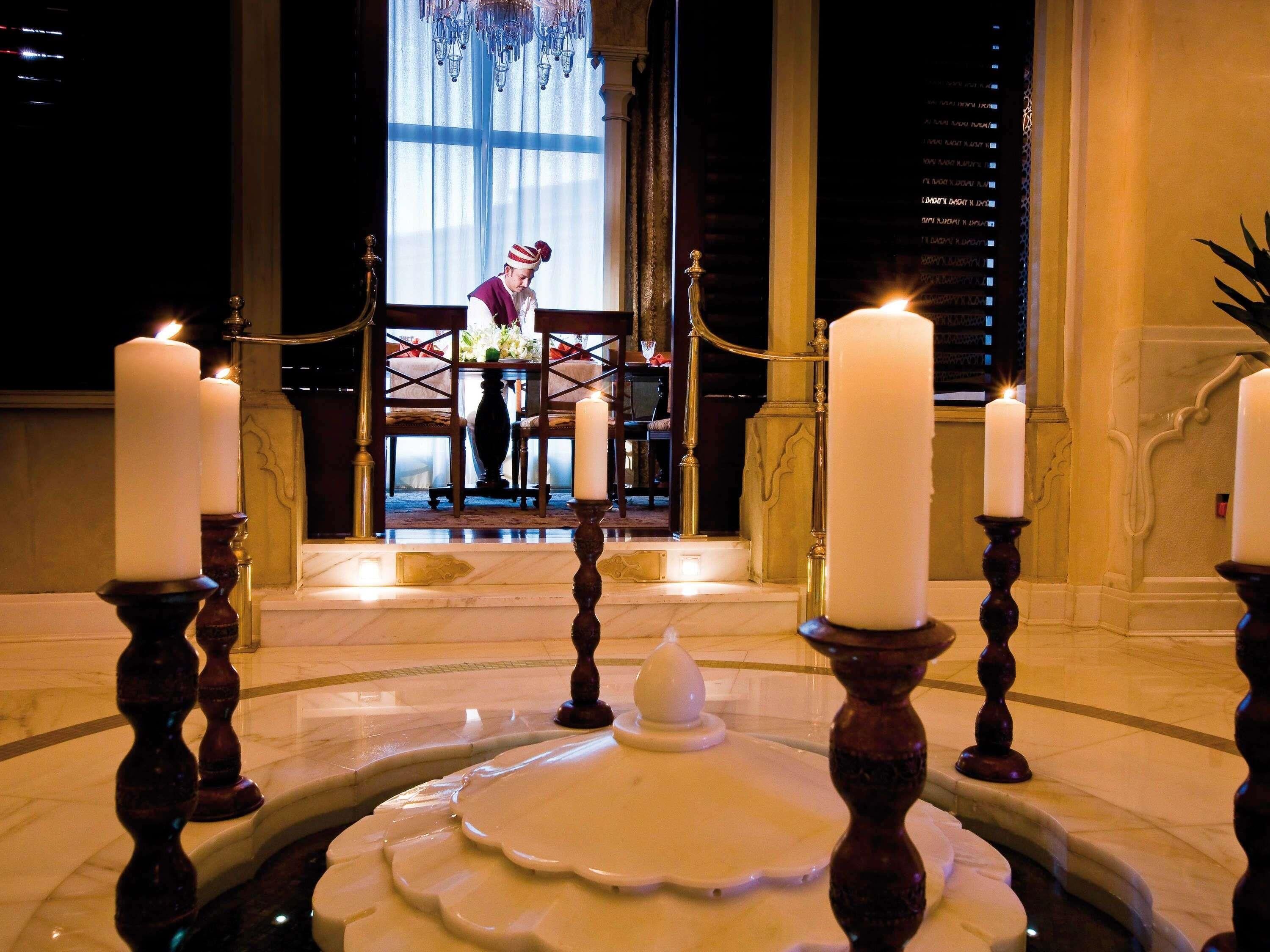 A room with a chandelier, a table with a vase, and a person in traditional attire.