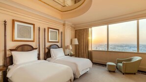 Habitación de hotel con dos camas, un ventanal amplio con vista a la ciudad, una silla y una lámpara.