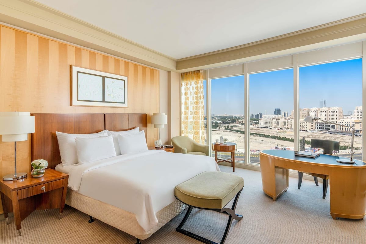A hotel room with a large bed, a desk, a chair, and a view of the city.