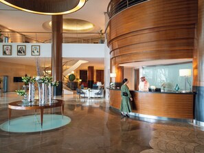 A modern hotel lobby with a reception desk, a staircase, and a seating area with a glass table. - Mövenpick Hotel Al Khobar (Al Khobar)