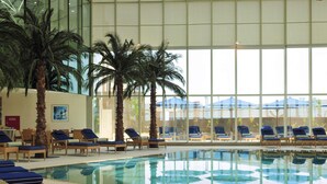 Una piscina interior con sillas de descanso y palmeras.