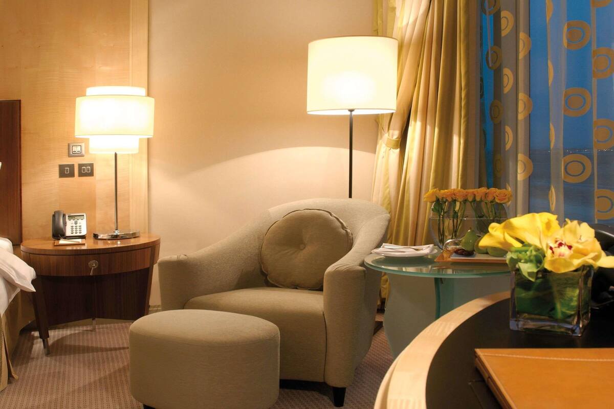 A hotel room with a sofa, a small table with a vase of flowers, a lamp, and a telephone on a side table.