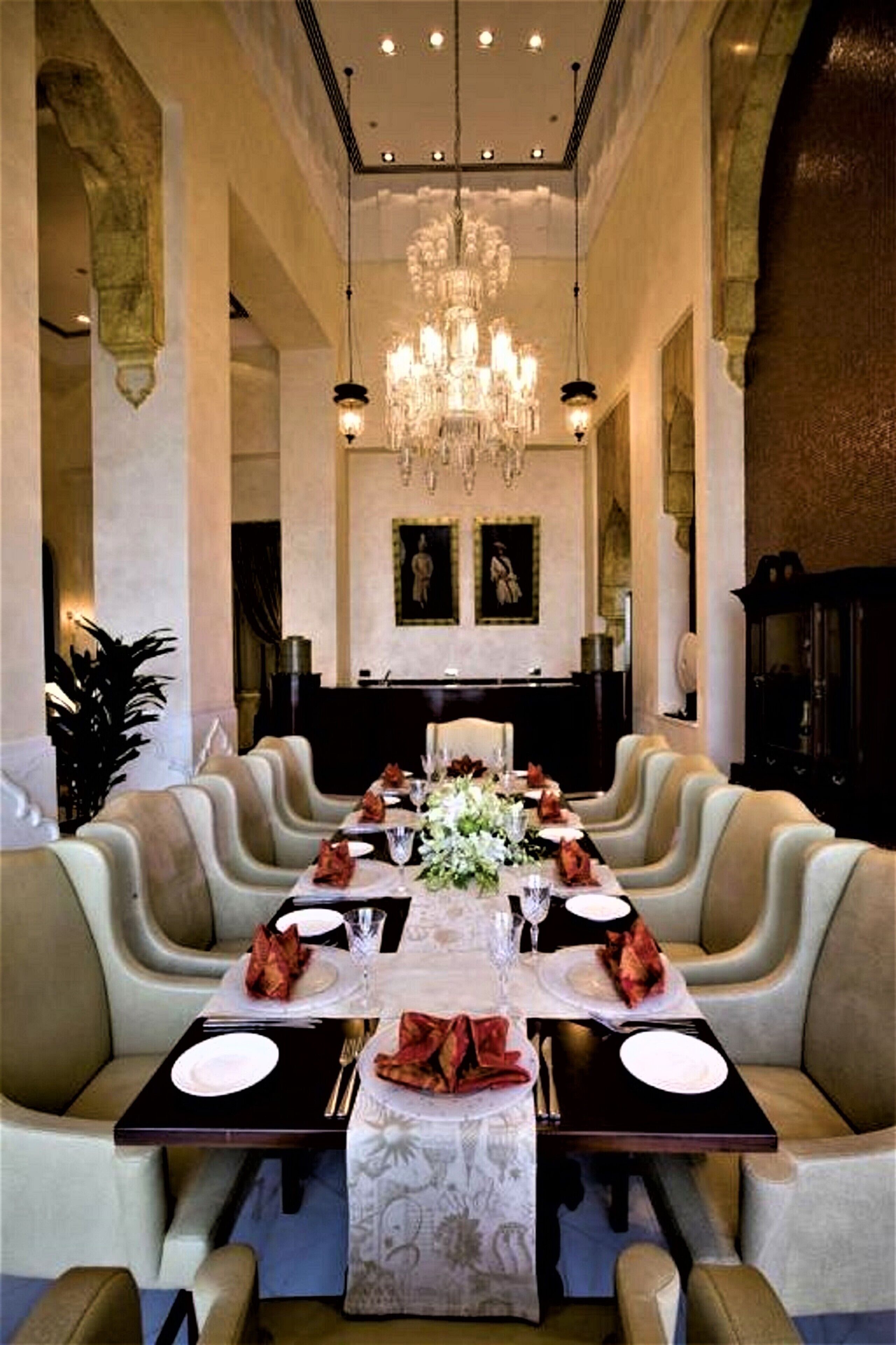 A formal dining room with a long table set for a meal, flanked by upholstered chairs, a chandelier, and framed artwork on the walls.