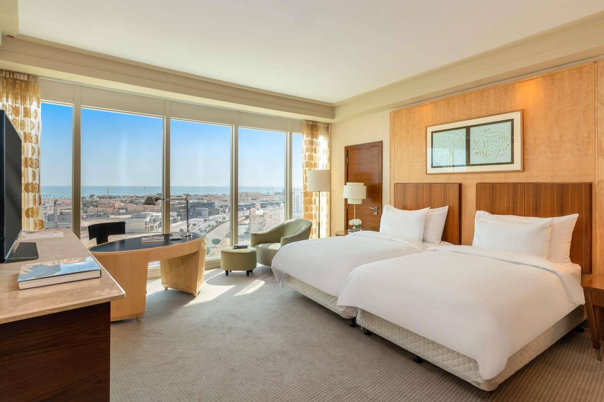 A hotel room with a large bed, a desk, a chair, a lamp, and a view of the city.