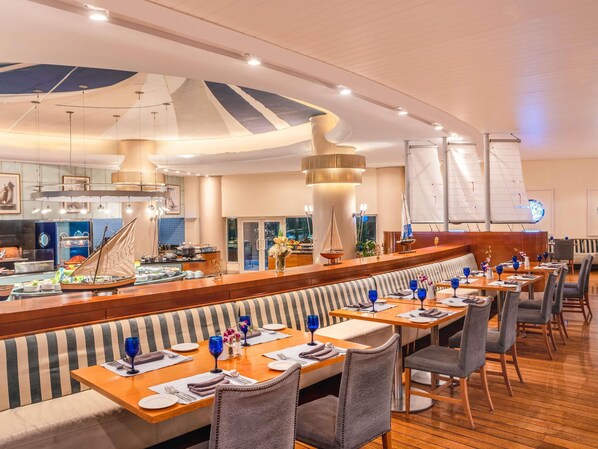 A restaurant with a long counter, striped seating, and sailboat decorations. - Mövenpick Hotel Al Khobar (Al Khobar)