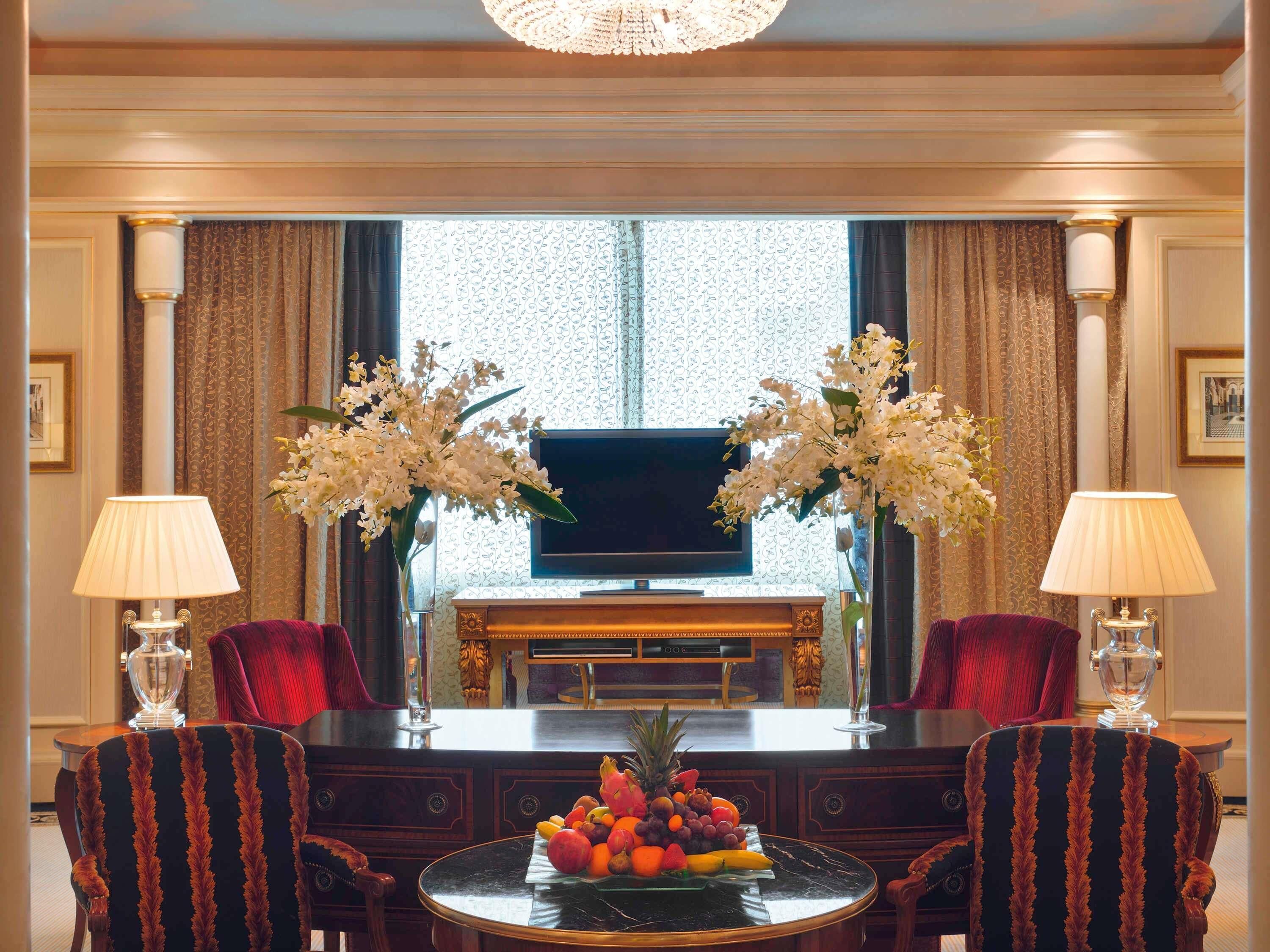 A room with a TV, two chairs, a table with fruit, and two lamps.