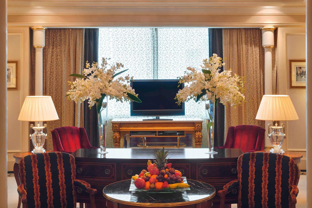 A room with a TV, two chairs, a table with fruit, and two lamps.