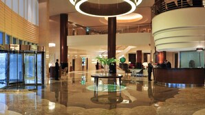 Un amplio vestíbulo con una fuente central, un mostrador de recepción y una escalera que conduce a un nivel superior.