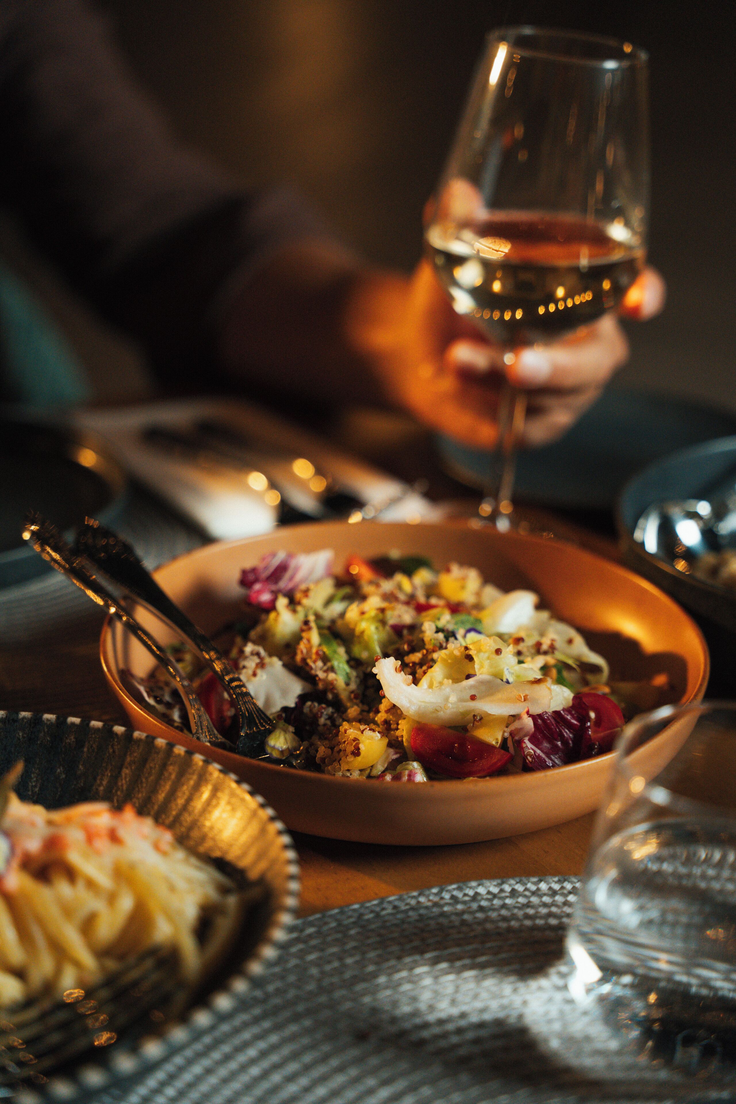 A dining table with a bowl of salad, a glass of wine, and a fork.