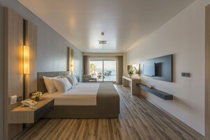 Habitación de hotel moderna con una cama grande, mesitas de noche, un televisor de pantalla plana y un balcón con vistas.
