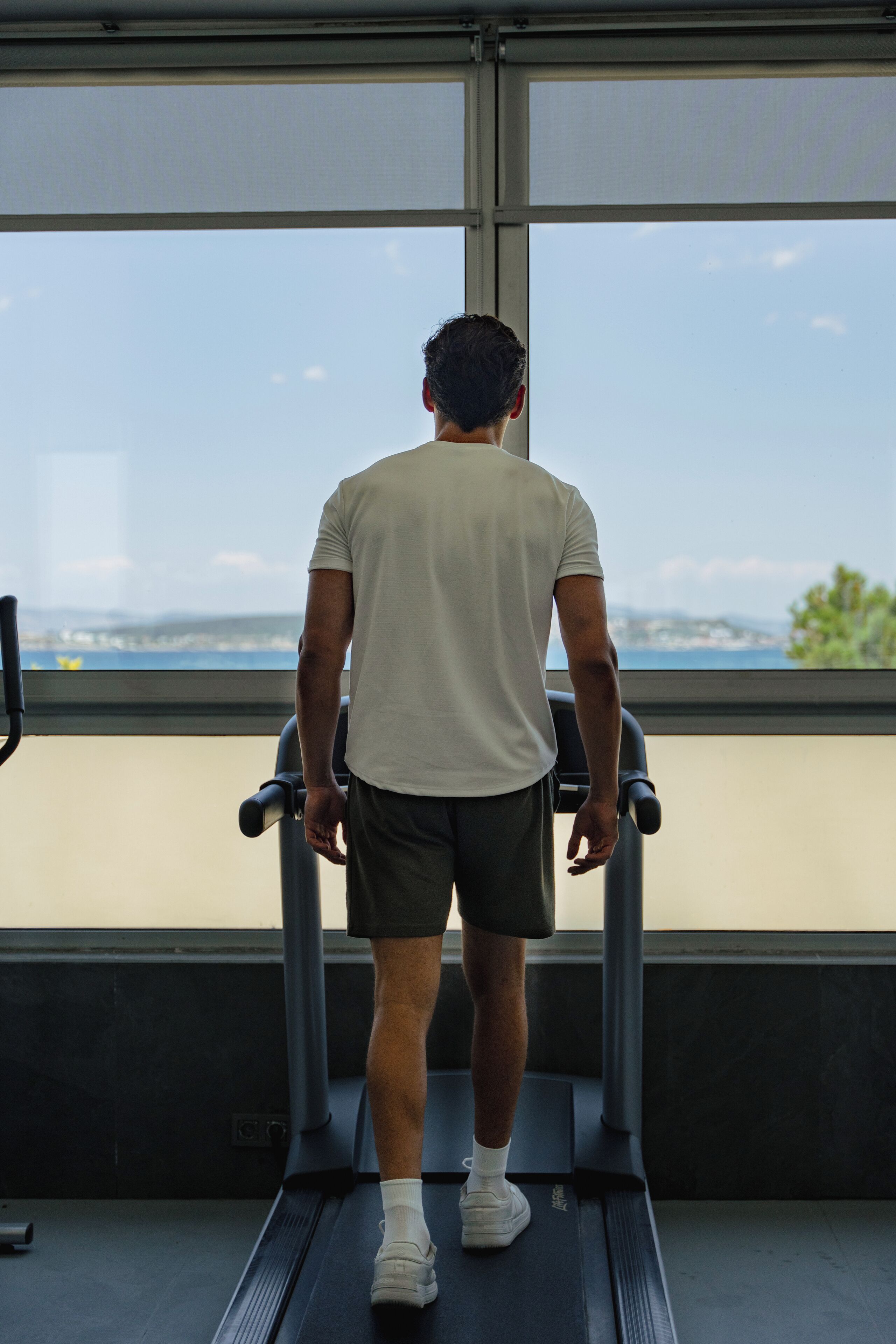 Un hombre camina en una cinta de correr en un gimnasio con vistas al mar y a las montañas.
