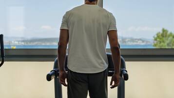 Un hombre camina en una cinta de correr en un gimnasio con vistas al mar y a las montañas.