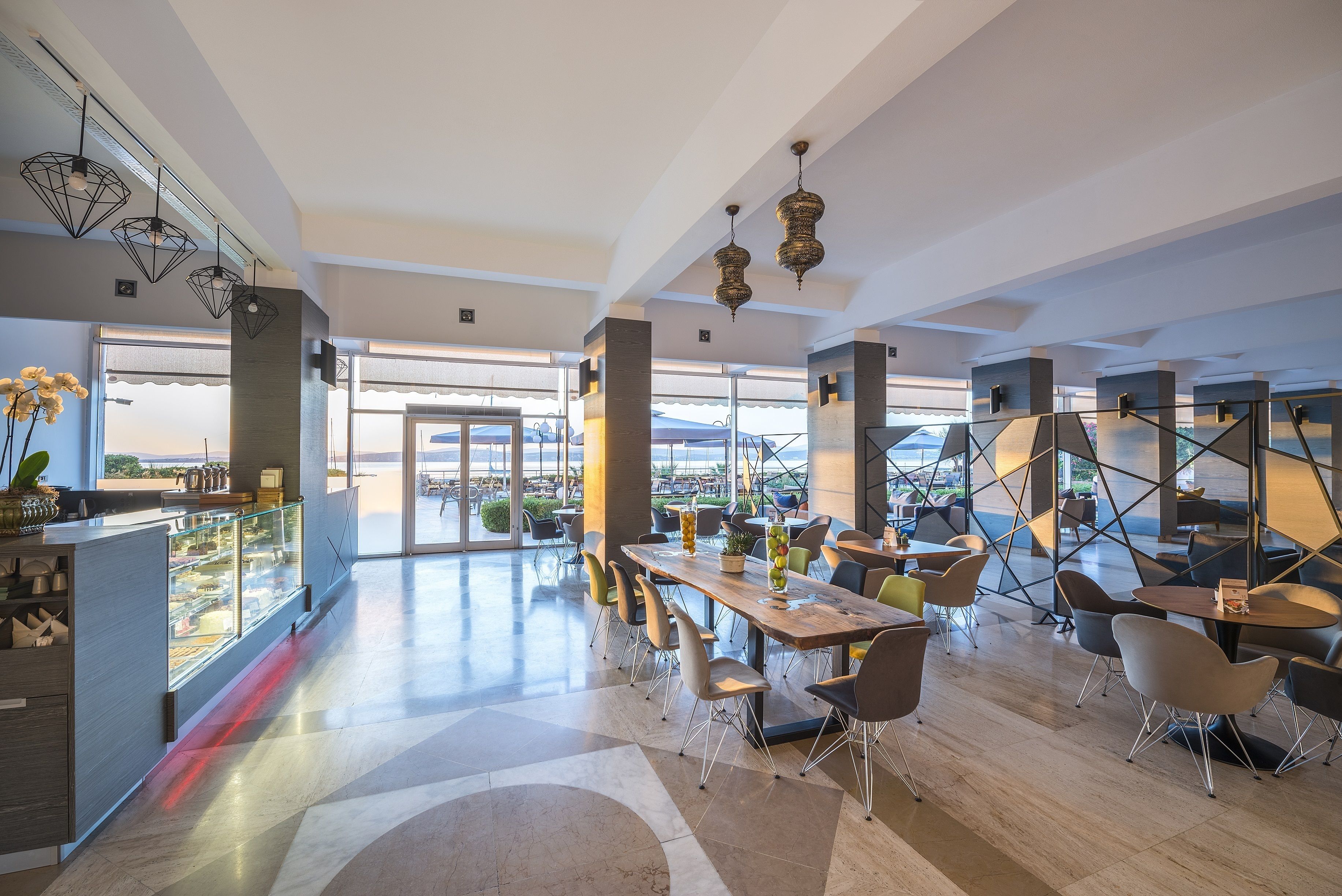 A spacious dining area with a long table and modern chairs, large windows offering a view, and decorative hanging lights.