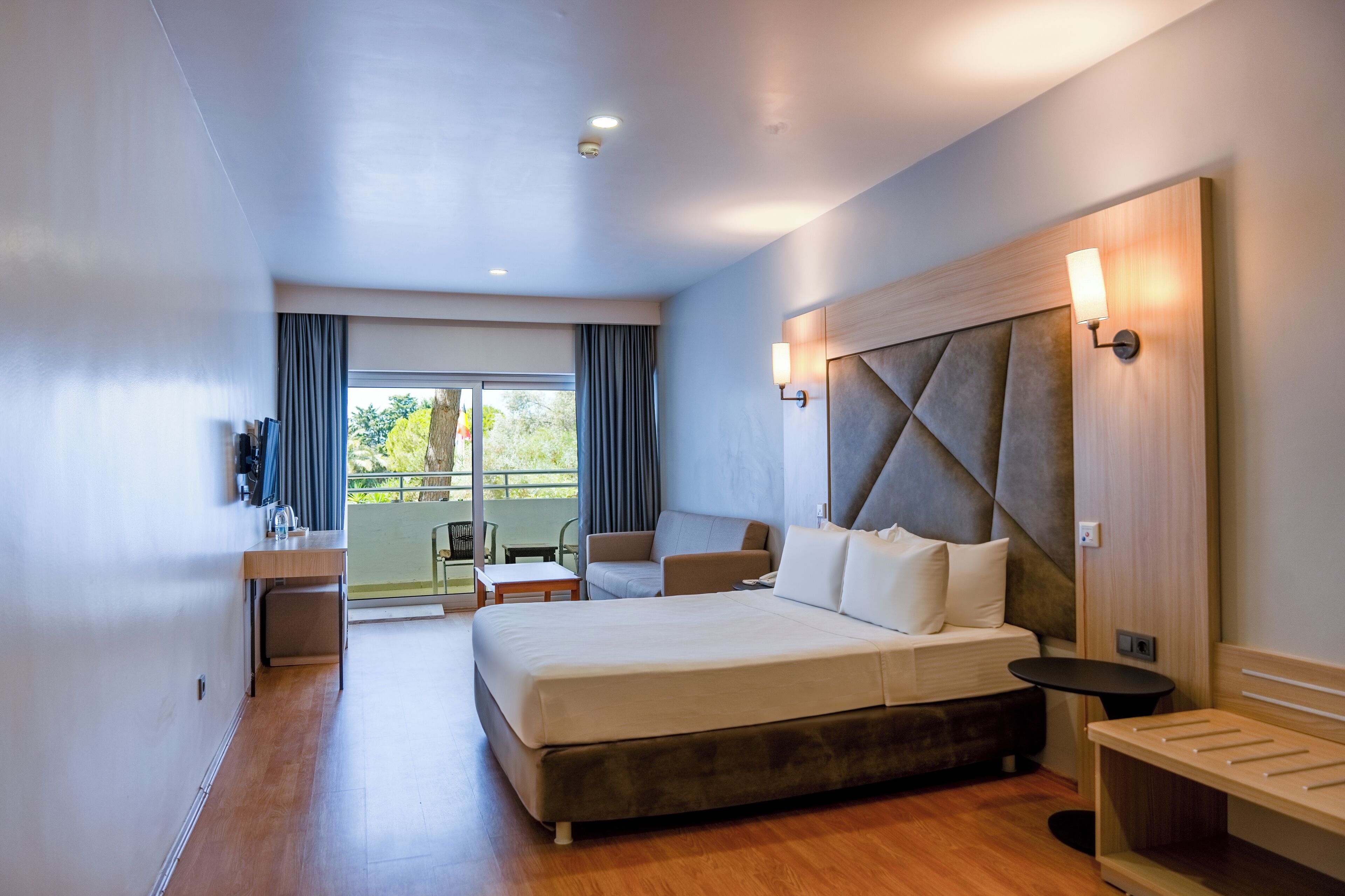 A modern hotel room with a large bed, a desk, a chair, and a balcony with a view.