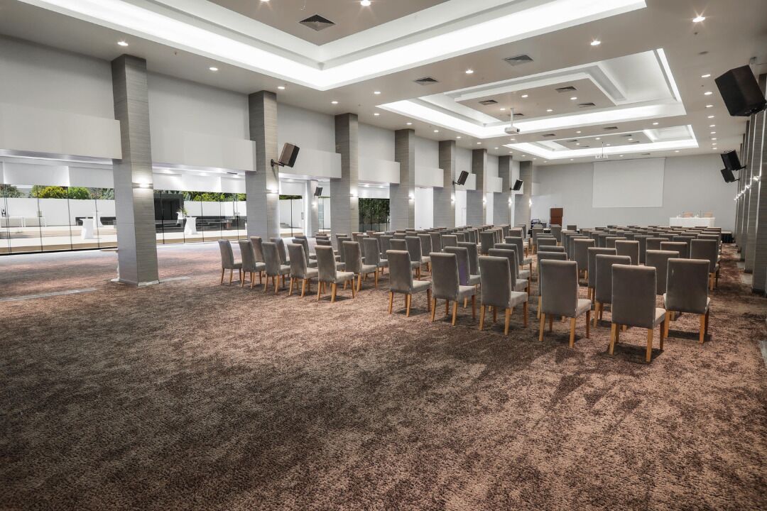 Un salón de conferencias con filas de sillas, piso alfombrado y un diseño moderno del techo.