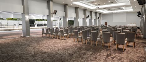 Un salón de conferencias con filas de sillas, piso alfombrado y un diseño moderno del techo.