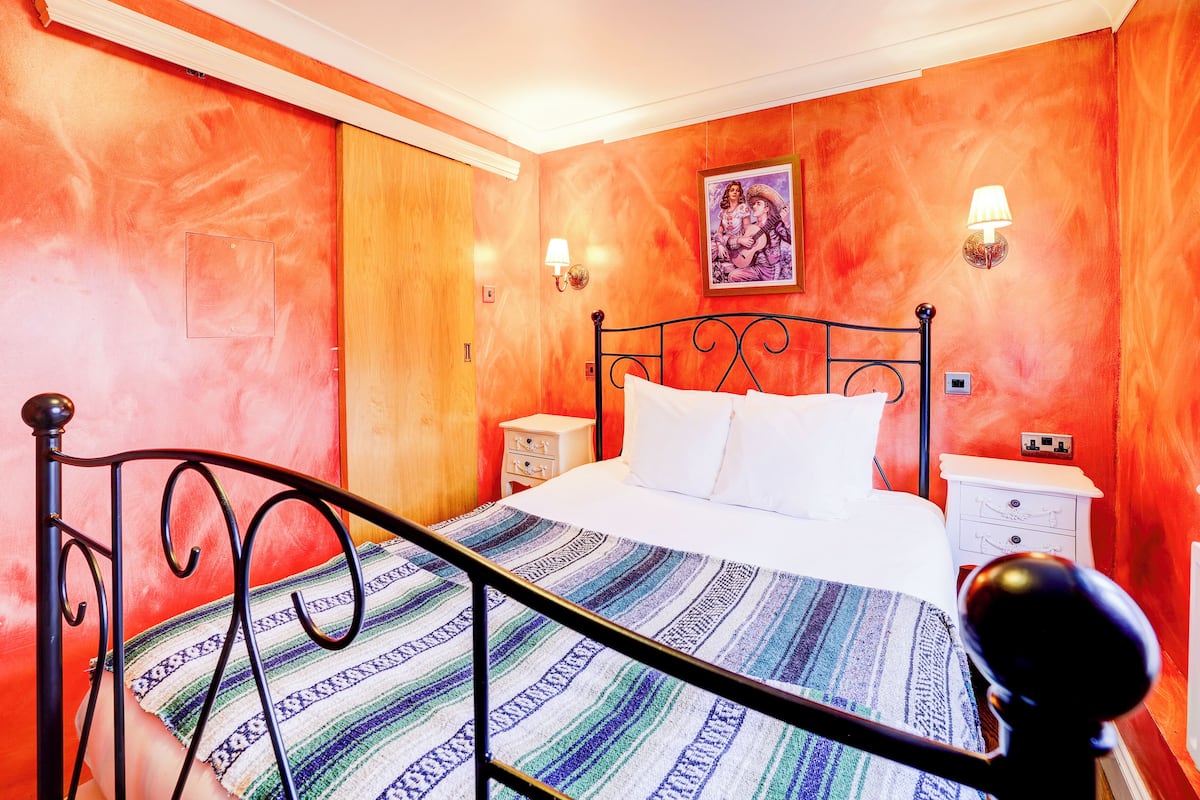 A bedroom with a bed, a nightstand, a wall-mounted lamp, and a painting.