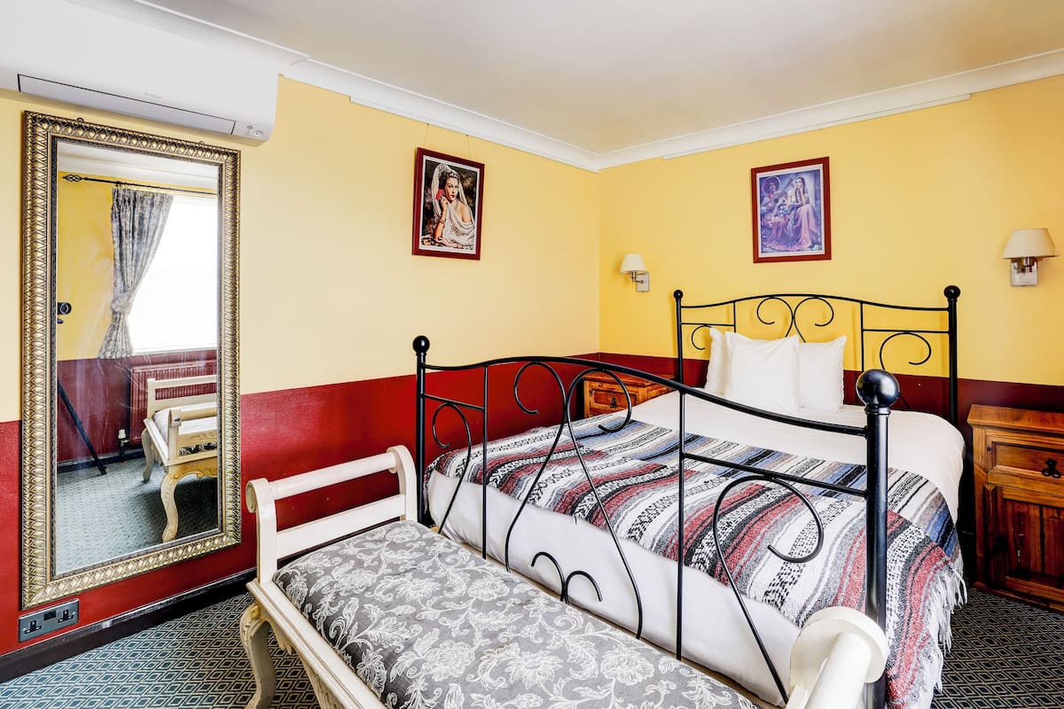 A hotel room with a bed, a bench, a mirror, and two wall-mounted lamps.