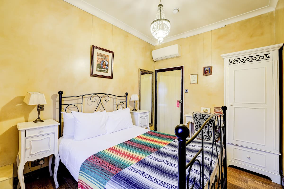 A hotel room with a bed, bedside tables, a chandelier, a wardrobe, and a framed picture on the wall.