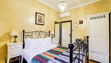 Quarto de hotel com cama, mesas de cabeceira, um candelabro, guarda-roupa e um quadro na parede.