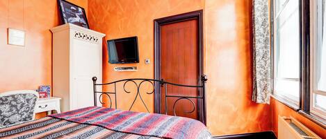 Un dormitorio con cama, armario, televisor y ventana con cortinas.