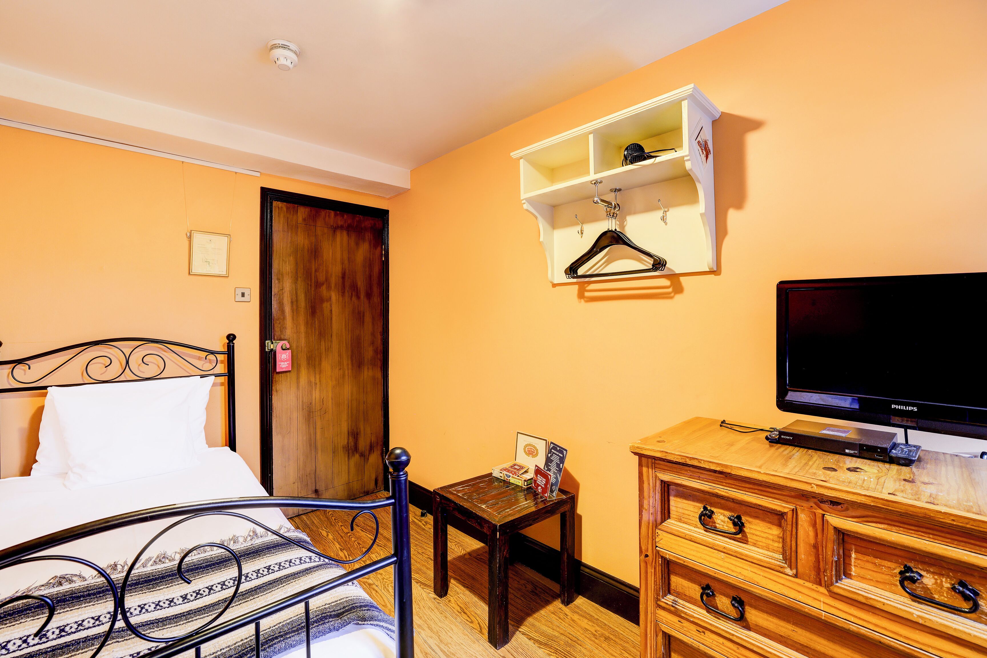 A hotel room with a bed, a television, a wooden dresser, and a small table with a book and a magazine.