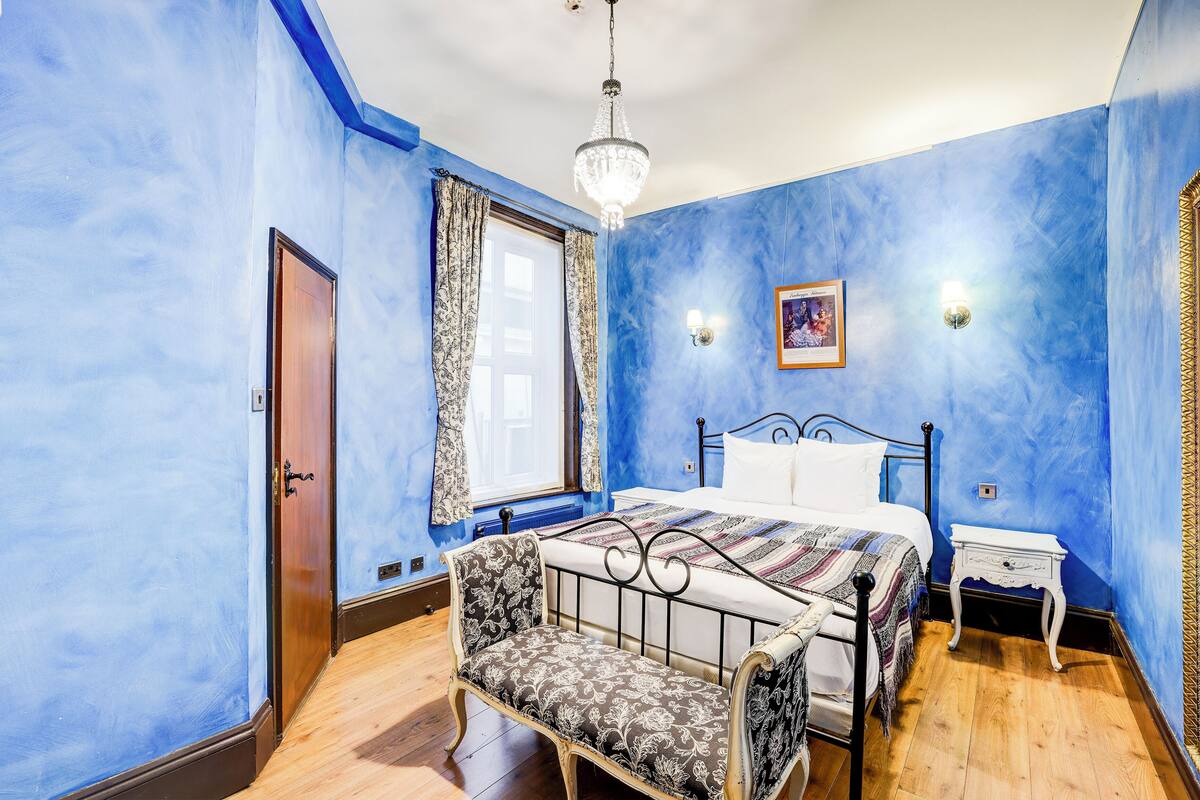 A bedroom with a bed, a chair, a nightstand, and a chandelier.