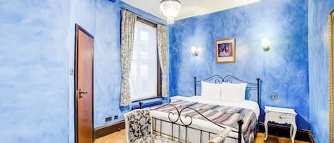 A bedroom with a bed, a chair, a nightstand, and a chandelier.