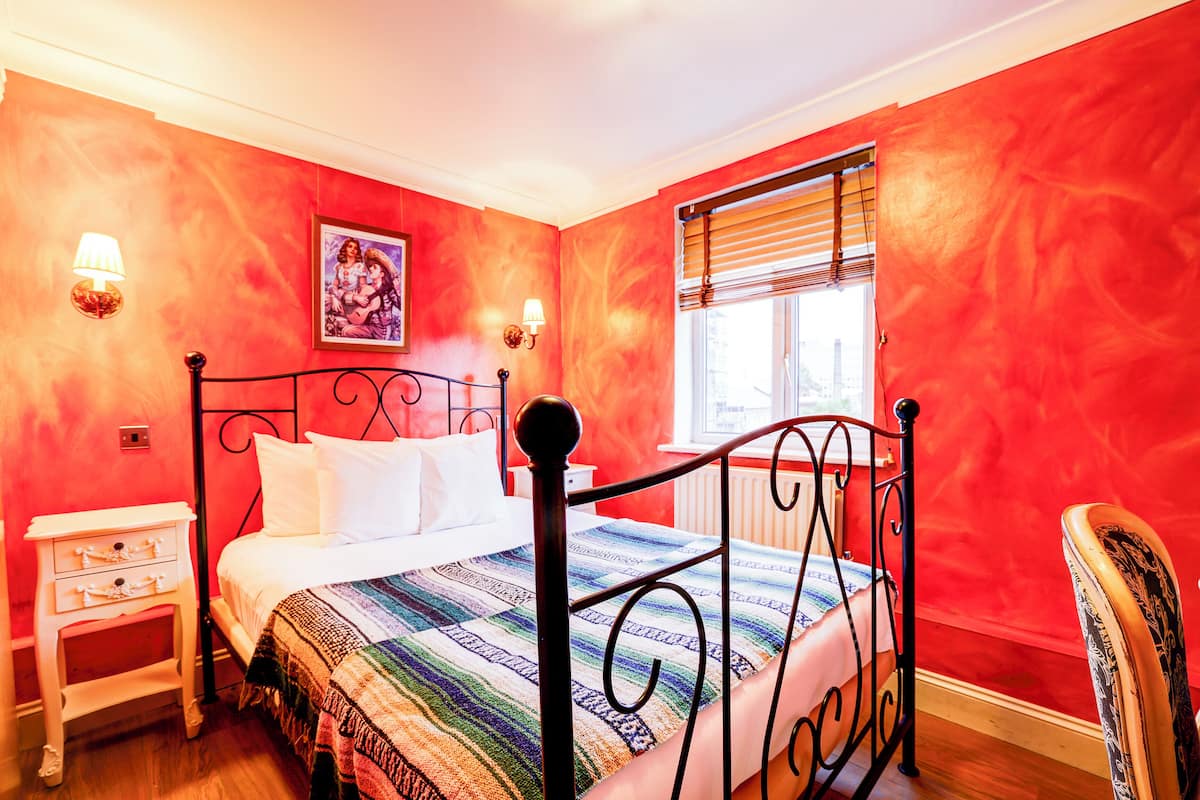 A bedroom with a bed, a nightstand, a chair, and a window with blinds.