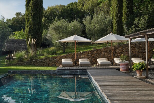Un área de piscina con muelle de madera, sillas de descanso y sombrillas.