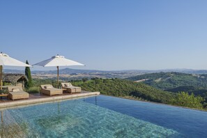 An infinity pool with lounge chairs and umbrellas, overlooking a mountainous landscape. - Castello Di Vicarello (Cinigiano)