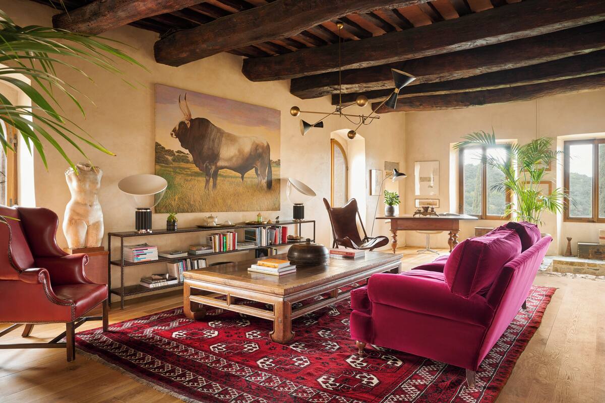 Un salón amplio con una mesa de centro de madera, un sillón rojo, un sofá morado y una alfombra estampada.