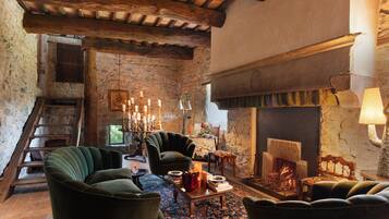 A rustic interior with a stone wall, wooden beams, a fireplace, and a cozy seating area.