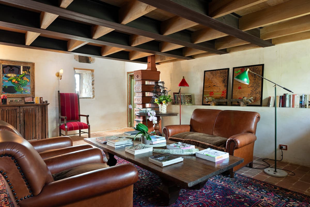 Una sala de estar acogedora con sillones de cuero, una mesa de centro de madera con libros, una lámpara roja y una estantería.