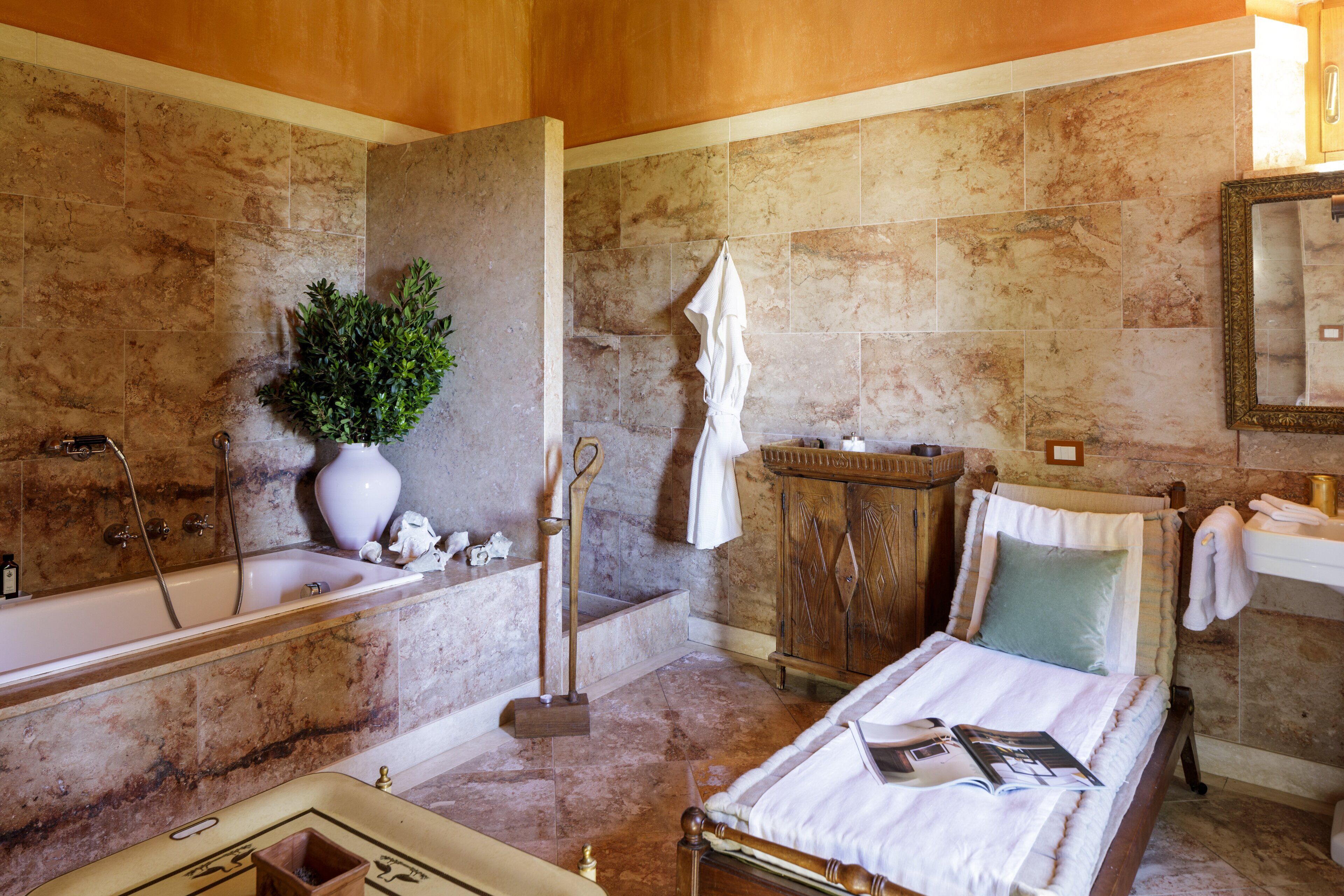 Une salle de bain avec une baignoire, un meuble en bois, un miroir et un lit sur lequel se trouve un magazine.