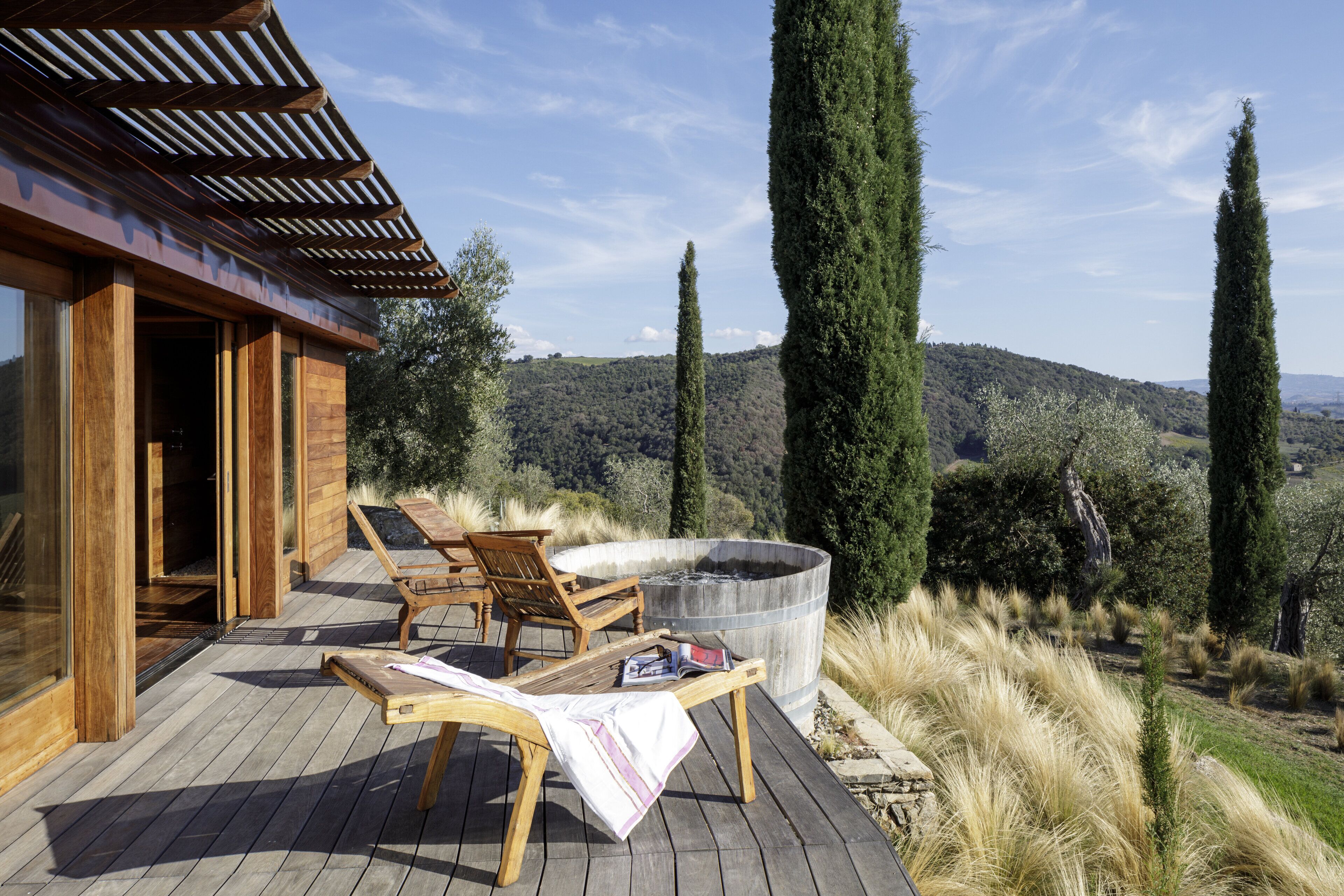 A wooden deck with lounge chairs and a hot tub overlooking a mountainous landscape.