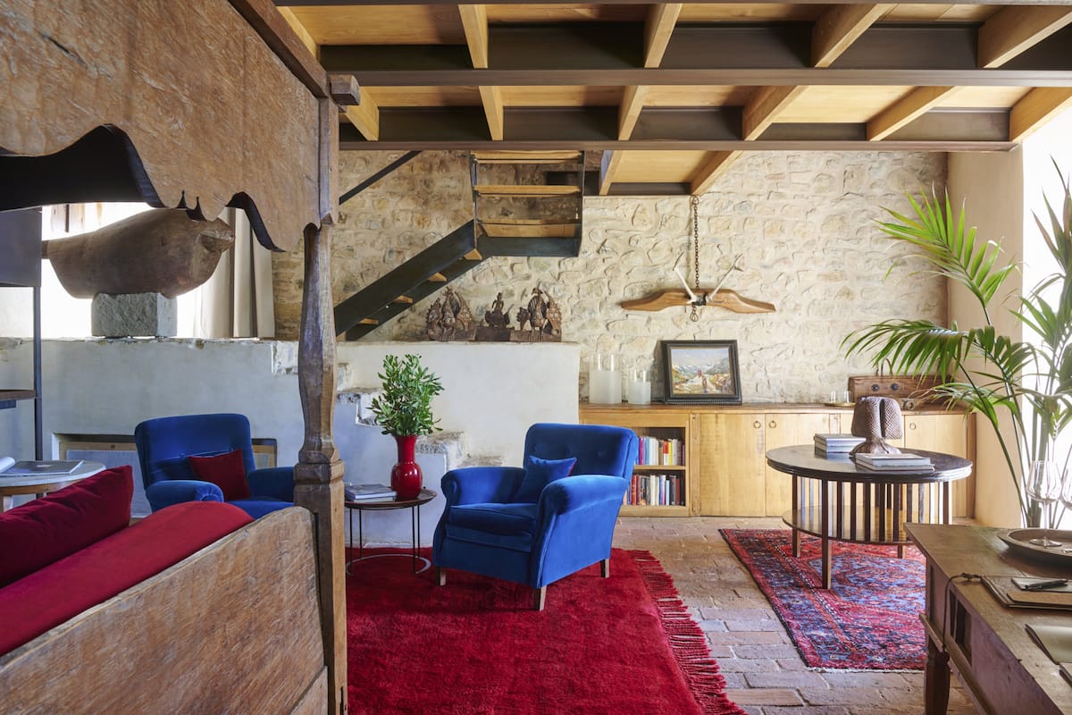 Un salón acogedor con alfombra roja, sillones azules, una mesa de centro de madera y una pared de piedra.