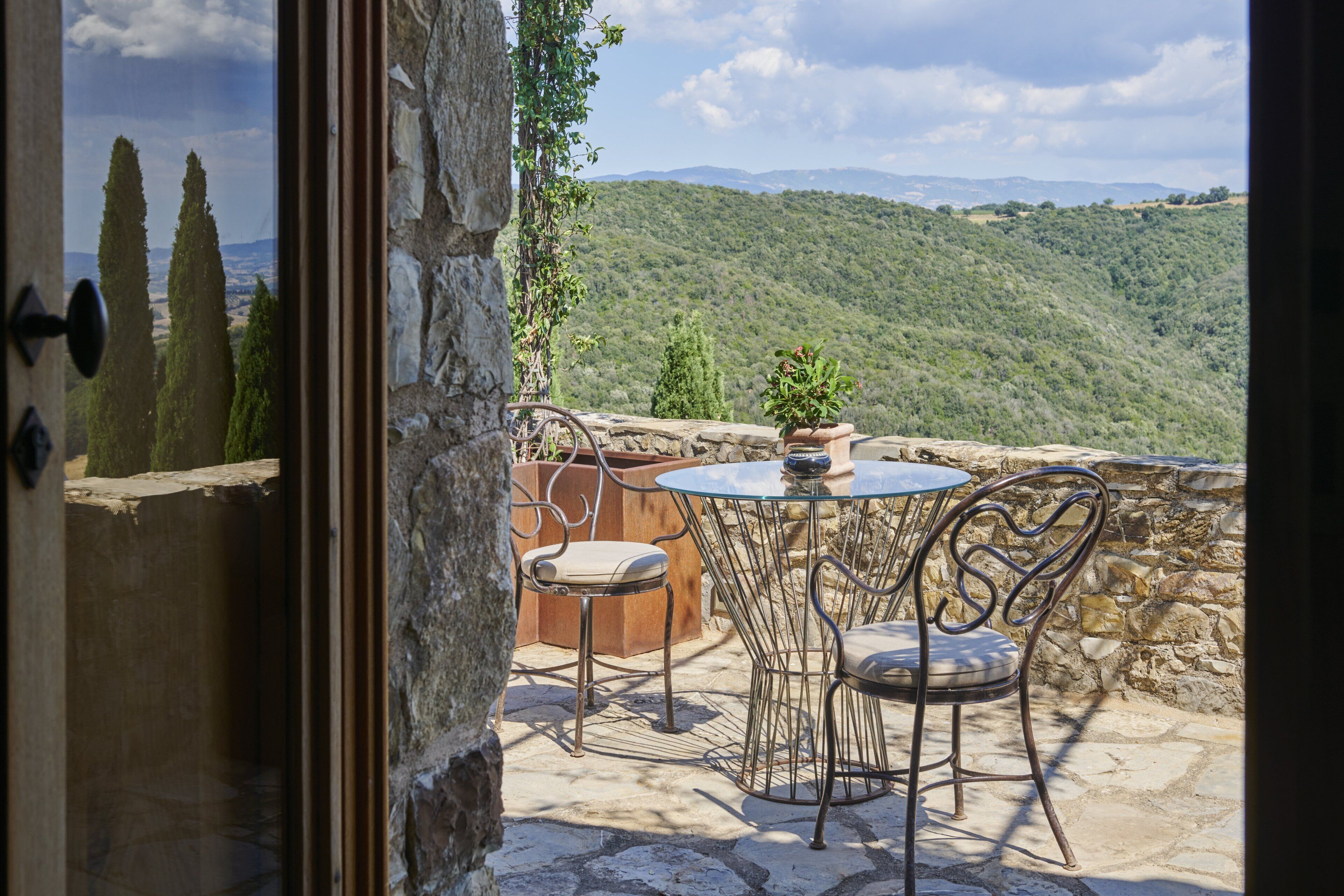 An outdoor patio with a stone table and metal chairs, overlooking a mountainous landscape.
