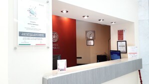 A hotel reception area with a red wall, a clock, and several framed certificates.